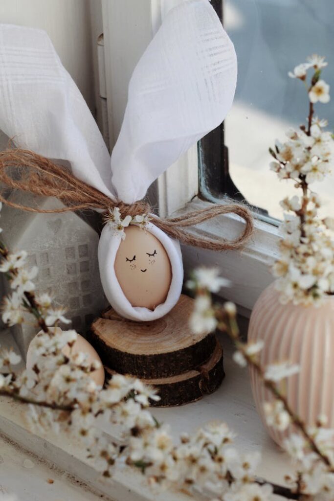 Charming Easter egg wrapped in cloth with bunny ears among spring blossoms on a windowsill.
